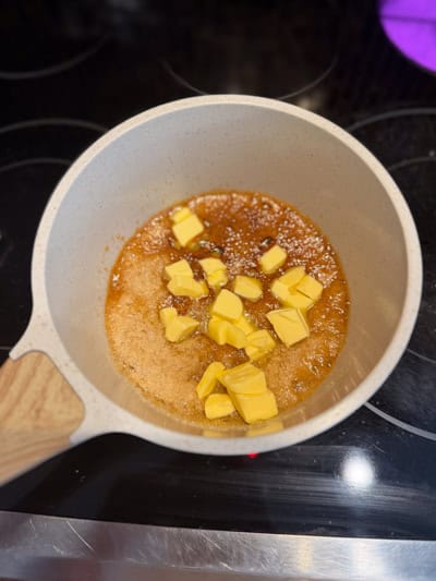 Dés de beurre salé ajoutés au caramel doré dans une casserole.
