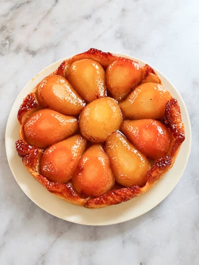 Tarte Tatin aux poires démoulée sur une assiette, dévoilant les fruits caramélisés et la pâte dorée.