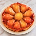 Tarte Tatin aux poires caramélisées et à la pâte feuilletée dorée, présentée sur une assiette crème.