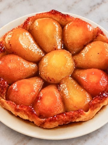 Tarte Tatin aux poires caramélisées et à la pâte feuilletée dorée, présentée sur une assiette crème.