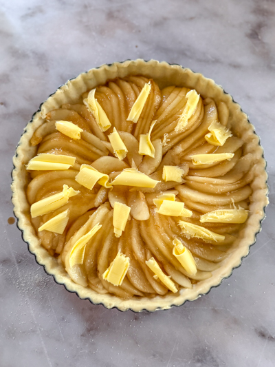 Tarte aux poires parsemée de sucre et de noisettes de beurre avant cuisson.